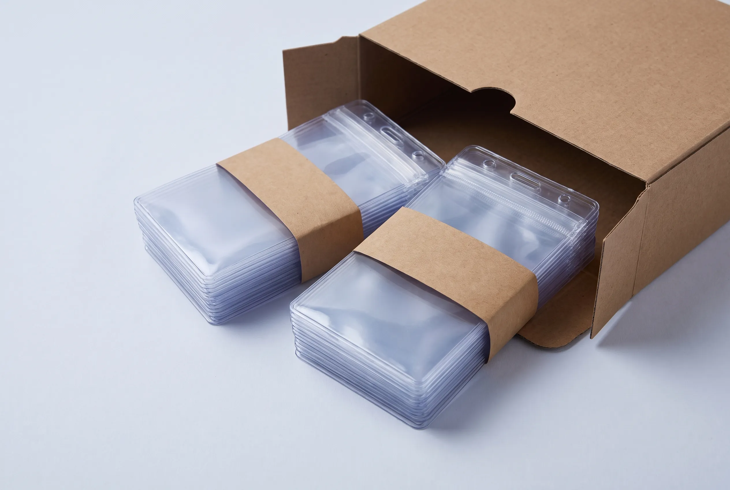 Banded bundles of clear lanyard pouches beside a plain cardboard box, ready for packing.