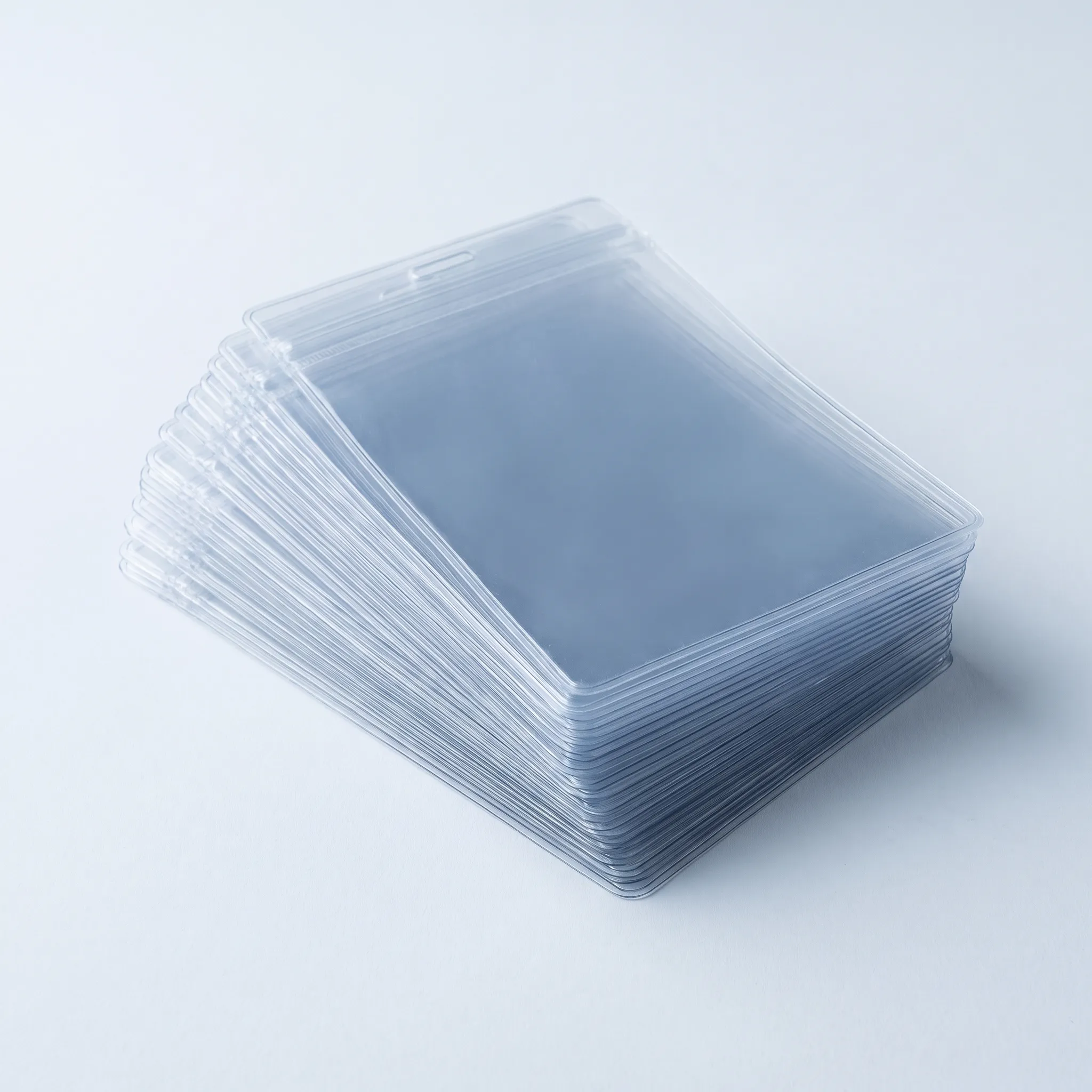 A stack of clear PVC lanyard pouches lying flat and slightly offset, the plastic deepening in tone where the layers overlap.