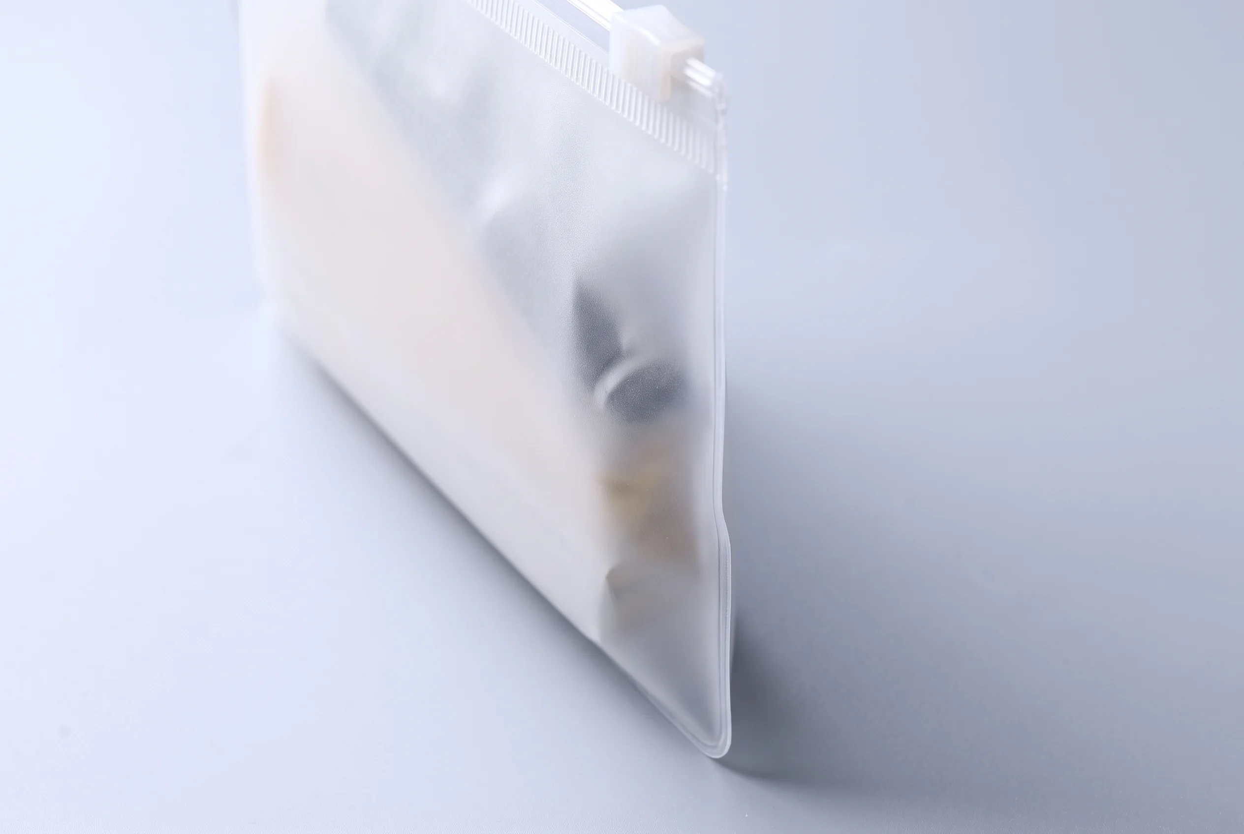 Close view along the sealed side edge of a frosted PVC zipper bag, showing the visible thickness of the 100 micron material as the bag stands upright without support.