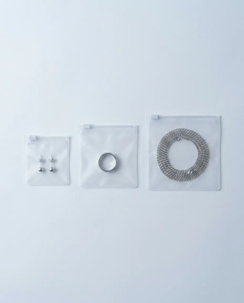 Three small frosted zipper bags at 5 by 5, 7 by 7 and 9 by 9 centimetres, each holding a simple piece of jewellery.